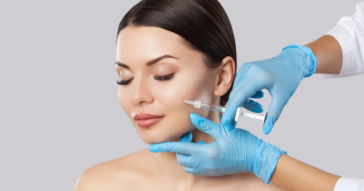 A woman receiving a dermal fillers injection in her cheek from a professional wearing blue medical gloves, highlighting a cosmetic facial enhancement procedure in Chicago, IL